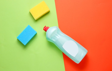 A bottle of detergent gel for dishes, sponges on a colored paper background. Top view