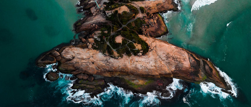 Rock formation on the coast of Rio de Janeiro locally known as Arpoador, harpooner, in the neighbourhood of Ipanema seen from above while ocean waves are crashing into it