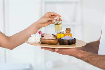 cropped view of woman taking bottle with oil while masseur holding tray