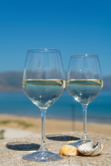 Two wine glasses with white wine served on outdoor terrace witn blue sea and mountains view on background