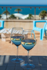 Two wine glasses with white wine served on outdoor terrace witn blue sea and mountains view on background