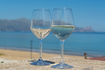 Two wine glasses with white wine served on outdoor terrace witn blue sea and mountains view on background