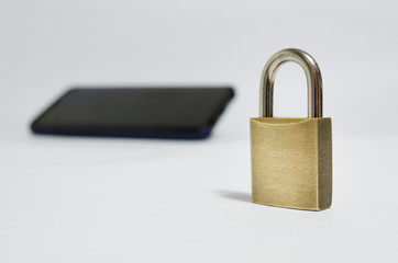 Conceptual photo security on mobile phones. A closed padlock in the foreground and a cell phone in the background on a white background.