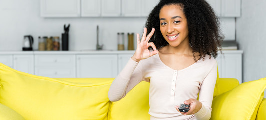 happy african american woman with remote controller in hand showing ok sign