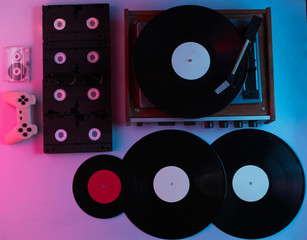 Retro media and entertainment items 80s. Vinyl player, Video, audio cassettes, 3D glasses, gamepad. Neon light. Top view