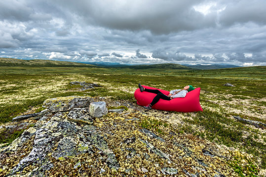 irl is relaxing in red airlounger, the desert landscape of Remdalen Valley in highlands of Oppland, Norway.