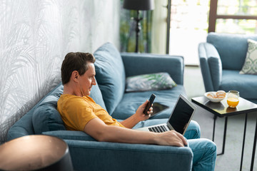 Adult man with smartphone sitting on sofa in room
