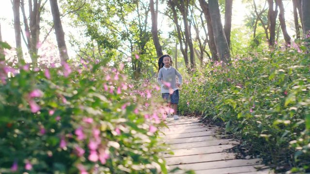 8 year-old beautiful little asian girl running on flagstone path through flower blossoms in park