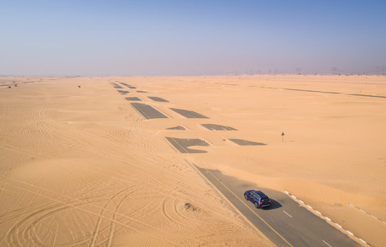 Aerial view of a car driving on a road covered with the sand of Dubai desert, U.A.E.