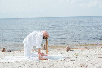 pretty woman with closed eyes practicing yoga on yoga mat near sea