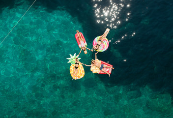Aerial view of group holding hands on inflatable mattresses on Atokos island, Greece.