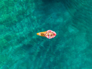 Aerial view of woman floating in bikini on inflatable ice-cream mattress on Atokos island, Greece.
