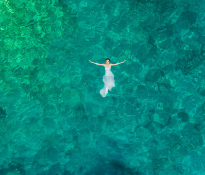 Aerial view of a woman floating in the sea of Atokos island using a wedding dress, Greece