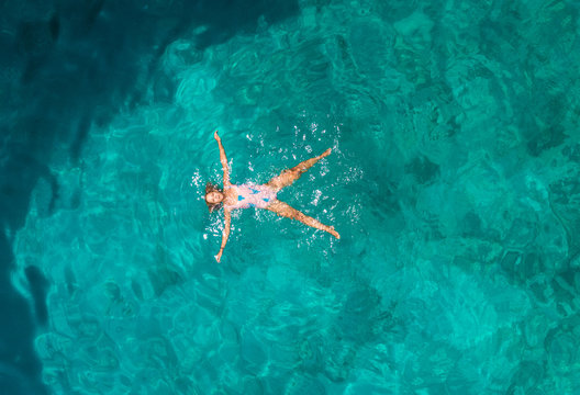 Aerial view of a attractive young woman in swimsuit floating in the sea off Atokos island, Greece