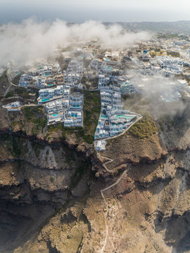 Aerial vertical view over the clouds of traditional white houses on Santorini island, Greece.