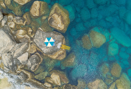 Aerial view of shore of Rhodes island with multicolored parasol and yellow ladder leading into sea, Greece.