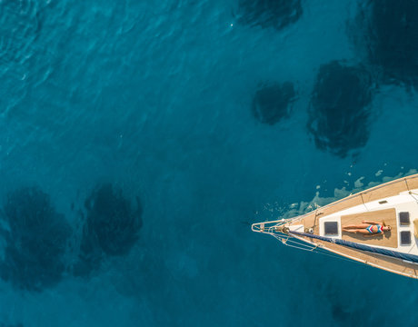 Aerial view of pretty woman in bikini sunbathing on deck of sailboat in the mediterranean sea, Greece.