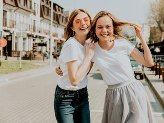 Portrait of two young beautiful blond smiling hipster girls in trendy summer white t-shirt clothes. Sexy carefree women posing on street background. Positive models having fun in sunglasses.Hugging