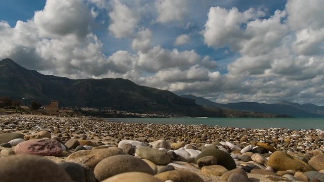 Sicily pebble beach during off-season. Surrounded by mountains, with fluffy clouds scudding over it. Time lapse.