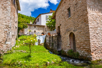 Fototapeta na wymiar The small village of Rasiglia, crossed by many streams and waterfalls, fed by the Menotre river. A sluice regulates the flow of water. Blooming white roses. Old brick houses. Foligno, Umbria.