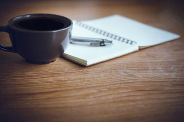 Closeup black cup with black coffee and notebook on wooden table. Vintage color tone