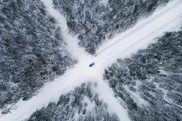 Aerial view of a blue car driving on a snowy forest road in Estonia.