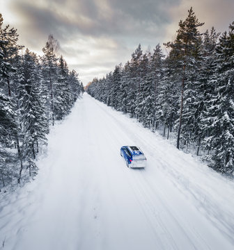 Aerial view of a blue car driving on a snowy straight forest road in Estonia.
