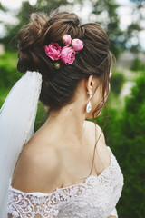 Obraz na płótnie Canvas Beautiful plus size model woman with stylish wedding hairstyle decorated with rose flowers in a fashionable wedding dress and in a veil posing outdoors