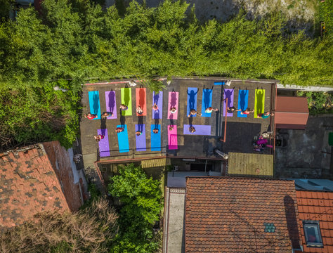 Aerial view of a group of people doing yoga on a terrace surrounded by trees in town