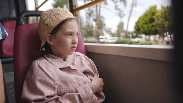 Little girl wrapped in a jacket on the bus with no Windows and looks outside.