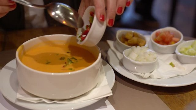 Preparing a bowl of spanish salmorejo or gazpacho by adding small pieces of fresh tomato, onion, pepper, cucumbers and even some crouton. Typical spanish tomato soup