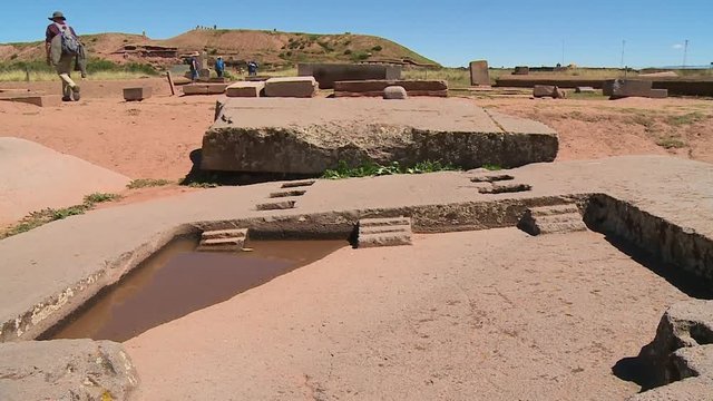 Close-up low angle tilting shot of an old stone carving replicating subterranean temple. A man is walking away from the site, Tiwanaku Ruins, Al Paz, Bolivia.