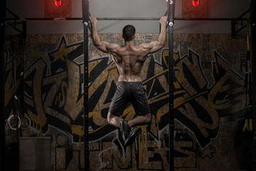 Athlete muscular fitness male model pulling up on horizontal bar in a gym