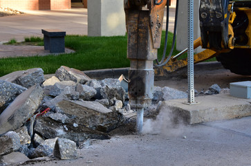 Backhoe with jackhammer tool breaking up concrete driveway.