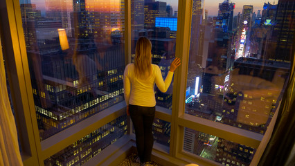 CLOSE UP: Female traveler stands by the window and observes Times Square at dawn