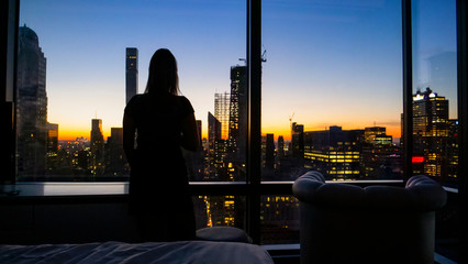 SILHOUETTE: Young woman watches the golden-lit cityscape of New York at dawn.