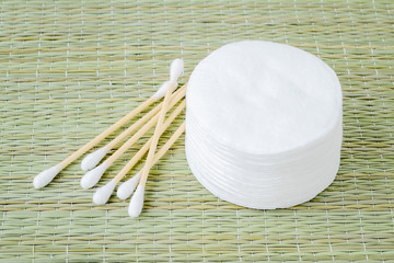 Stack of cotton pads and heap of wood stick cotton buds on a background of rough wicker mat made of...