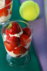 Whipped cream and strawberries served in a glass. Purple and dark green napkins, white wooden table, tennis ball, high resolution