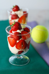 Whipped cream and strawberries served in a glass. Purple and dark green napkins, white wooden table, tennis ball, high resolution