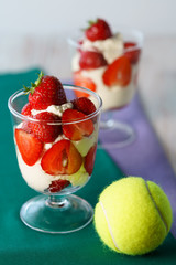 Whipped cream and strawberries served in a glass. Purple and dark green napkins, white wooden table, tennis ball, high resolution