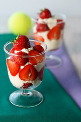 Whipped cream and strawberries served in a glass. Purple and dark green napkins, white wooden table, tennis ball, high resolution