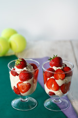 Whipped cream and strawberries served in a glass. Purple and dark green napkins, white wooden table, tennis ball, high resolution