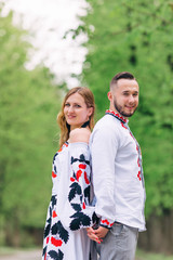 Newlyweds in embroidered clothes stand back to back and smile. p