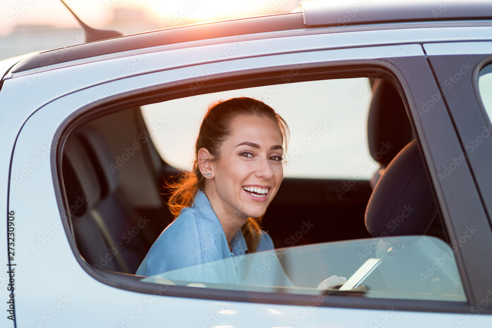 Wall mural Young woman with smartphone on the back seat of a car