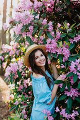 Portrait of young beautiful woman in straw hat posing among blooming trees