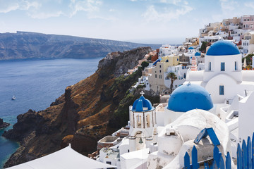 Fototapeta premium Niebieskie kopuły i dzwonnica kościołów w Oia, Santorini, Grecja. Krawędź kaldery z niebieskimi kopułami kościołów na pierwszym planie, selektywna ostrość