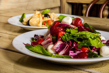 two dishes with salads of fried chicken, olives, basil, red pepper and lettuce, red cabbage, mozzarella, strawberry