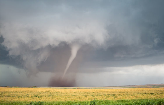 A thin cone tornado spins over the open landscape of the Great Plains.