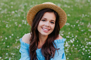 beautiful young brunette woman in straw hat on the meadow with white flowers on a warm summer day