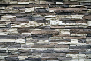 Stone wall texture background of narrow flat stones in brown, gray,beige colors
